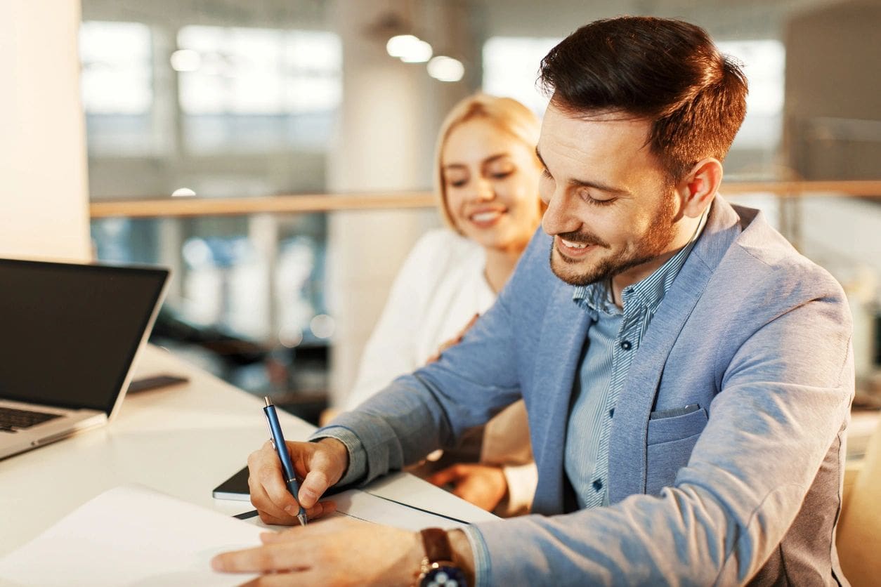 Man signing document with woman nearby.